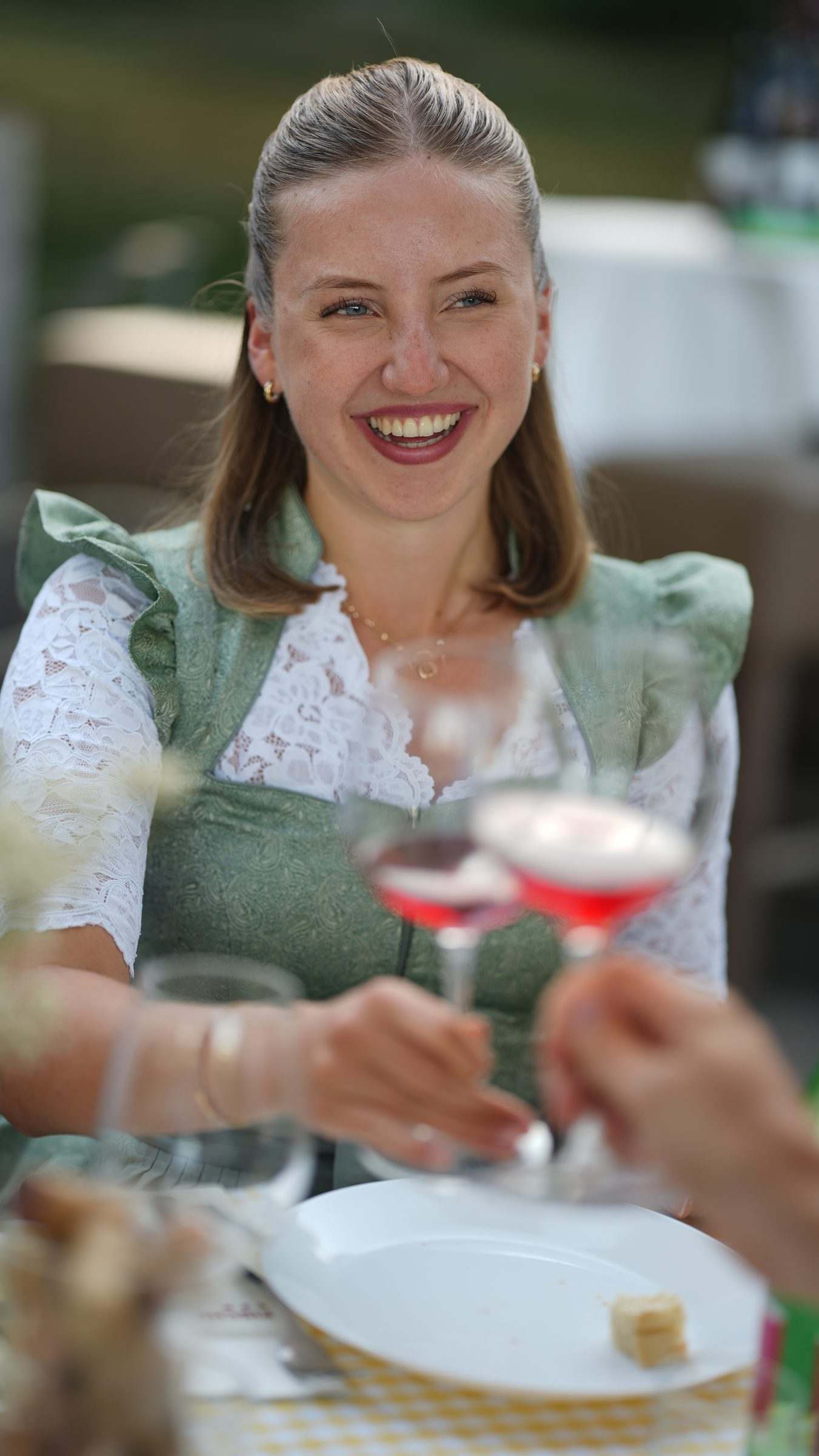 Frau im Dirndl stößt lachend mit Rosé an