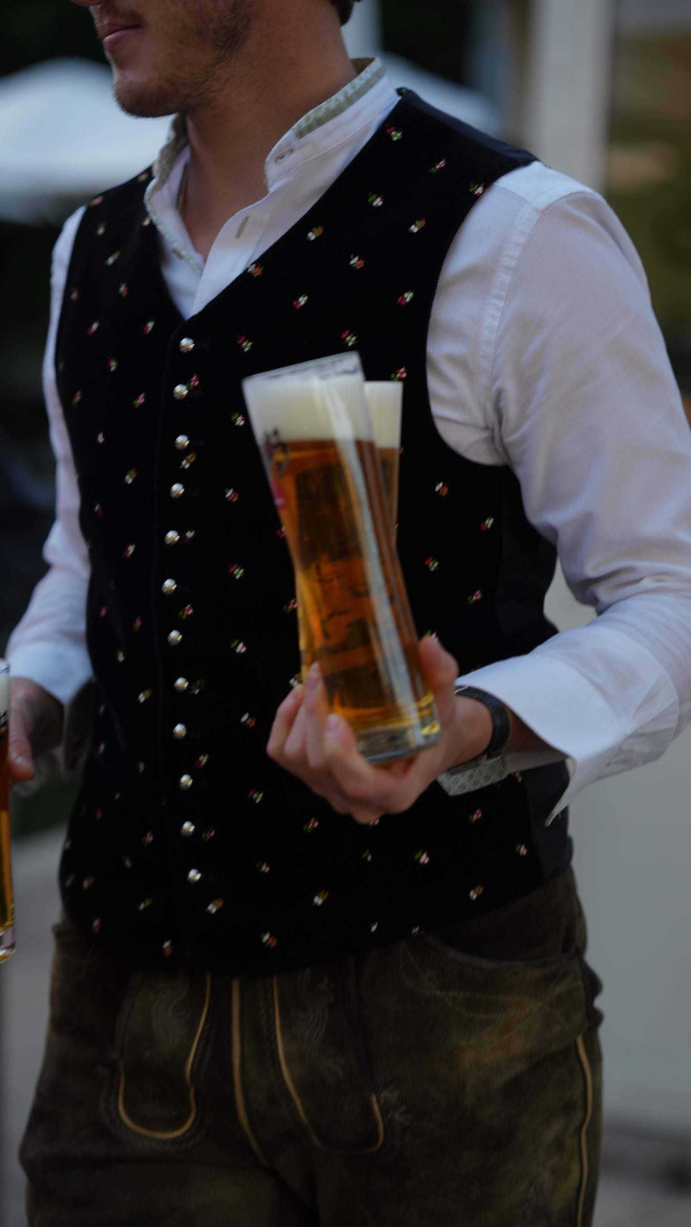 Kellner in Trachtenweste und Lederhose trägt ein frisch gezapftes Bier
