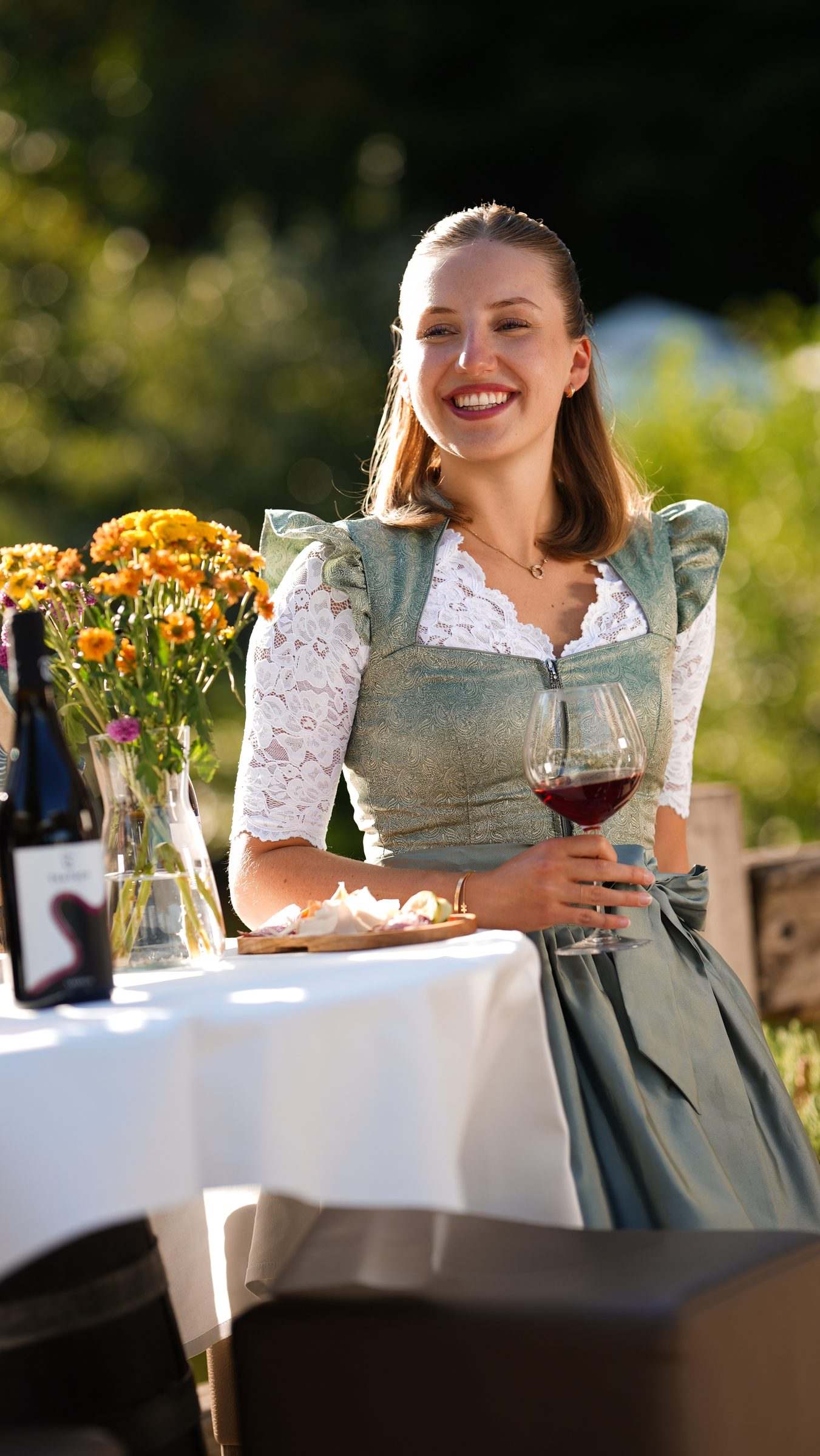 Frau im Dirndl mit Rotwein vor einem Herbststrauß