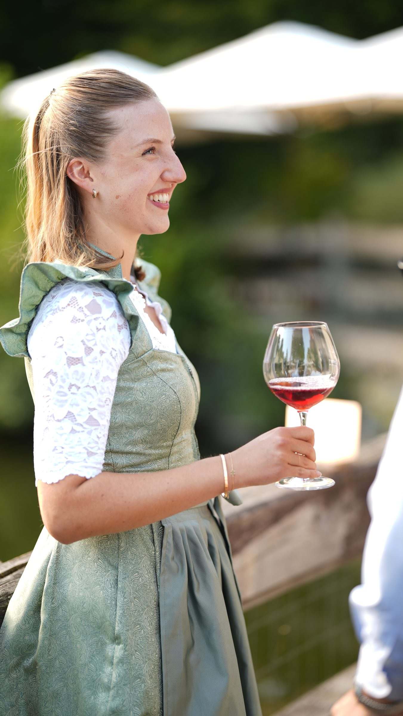 Frau im Dirndl mit einem Glas Rotwein am Teich