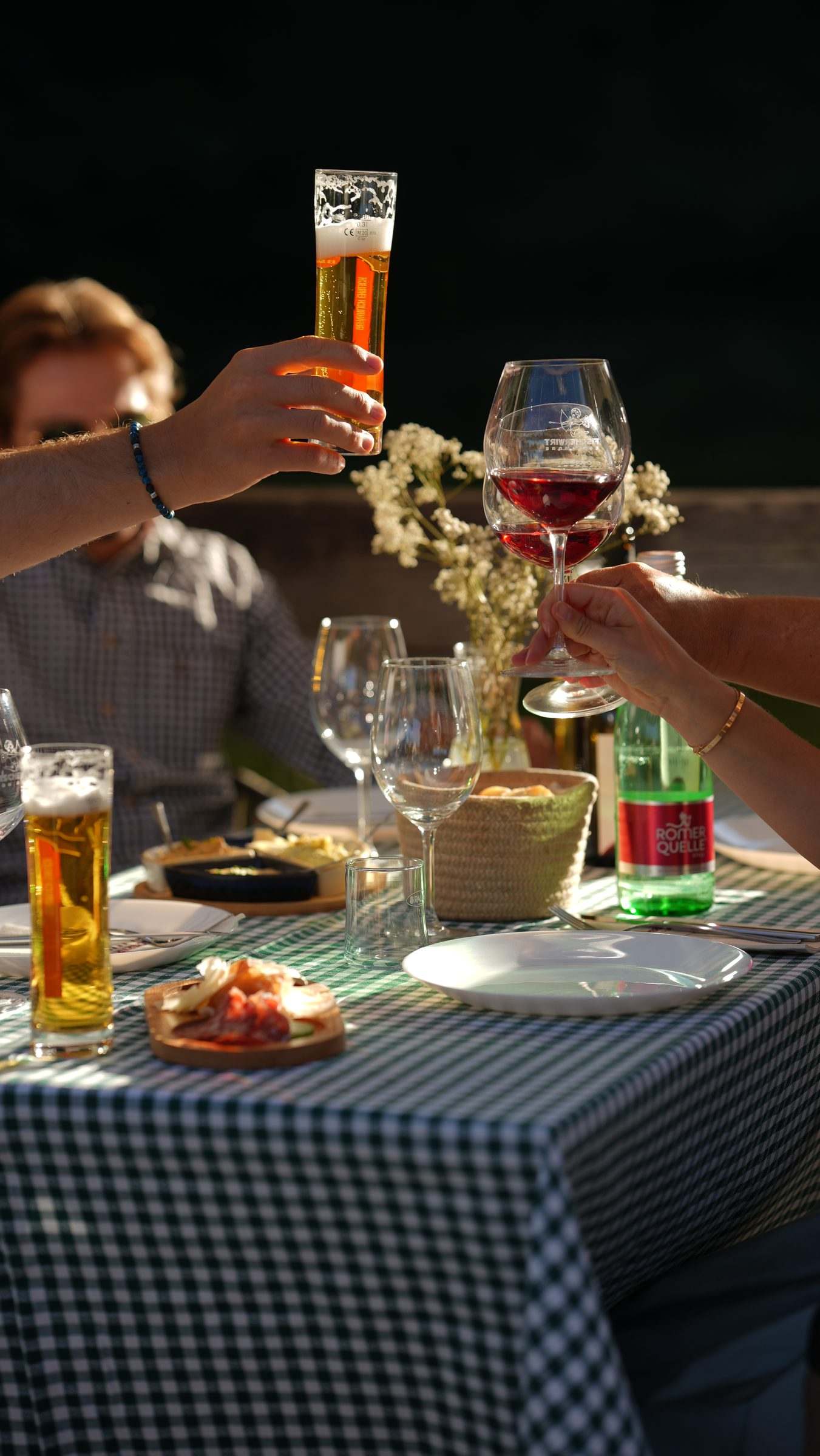 Gäste stoßen am grün karierten Tisch mit Bier und Rotwein an