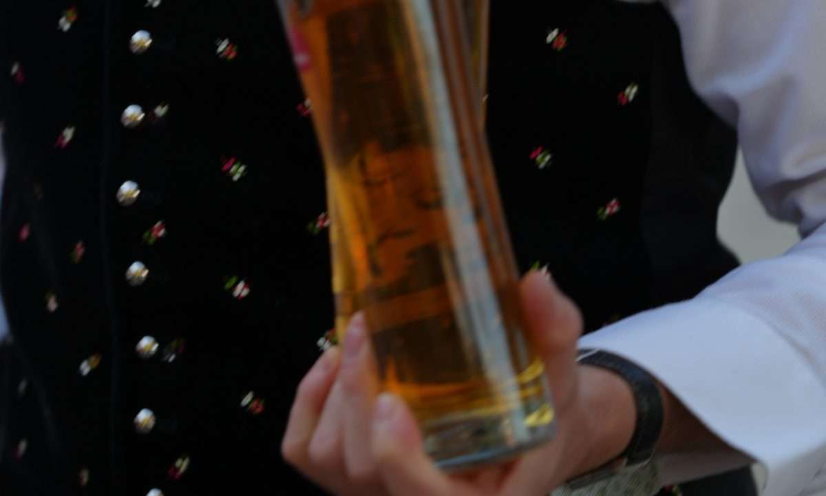 Frisch gezapftes Bier in hohen Gläsern, getragen von einem Kellner in Tracht