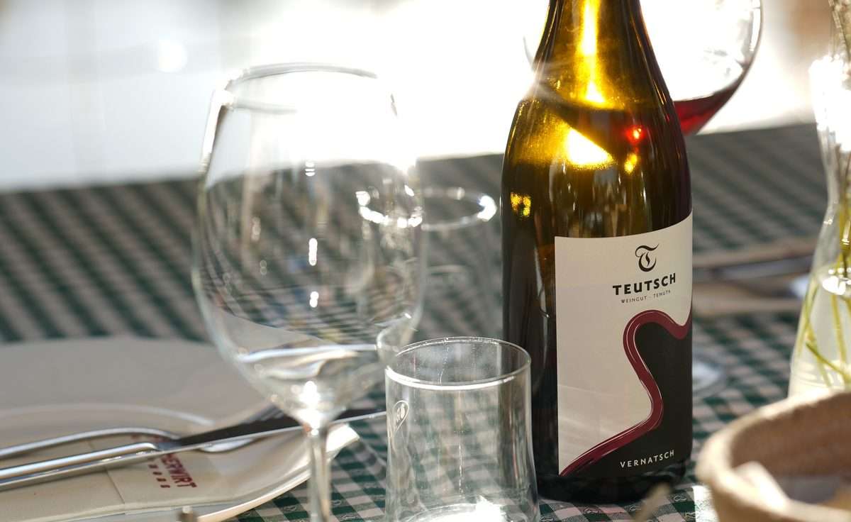 Rotweinflasche vom Weingut Teutsch neben Gläsern auf grün kariertem Tischtuch