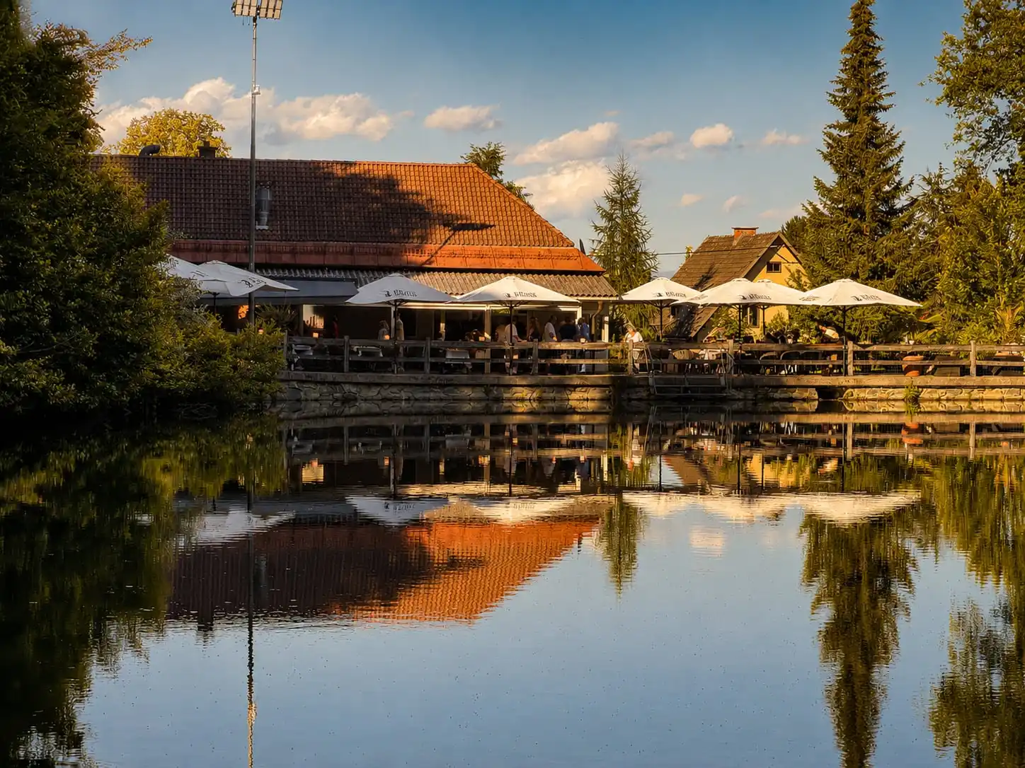 Fischerwirt con amore am Kreuzbergl in Klagenfurt – Abendsonne über der Terrasse am Teich, Spiegelung im Wasser