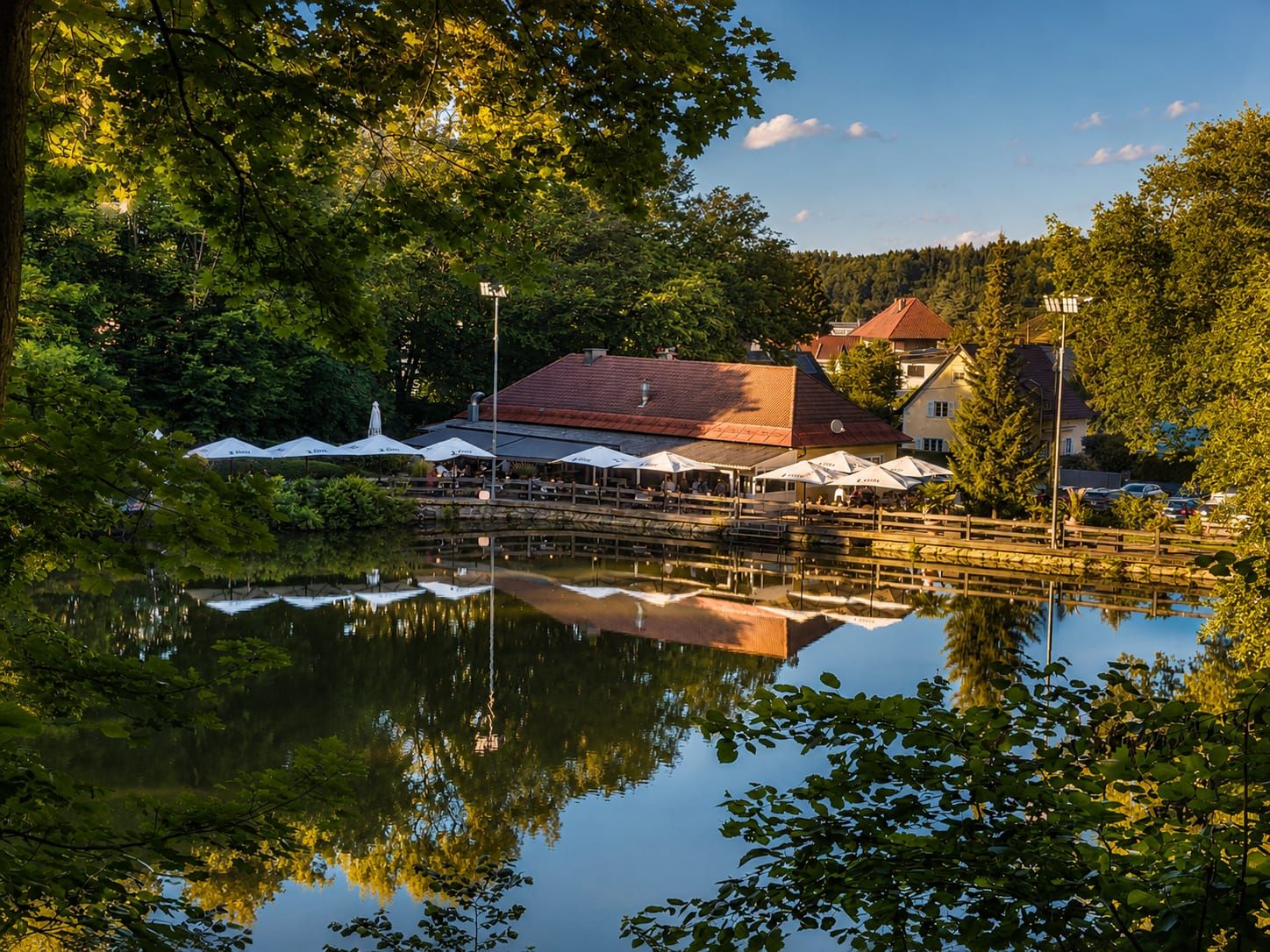 Terrasse des Fischerwirt con amore am Teich, eingerahmt von Grün – Sommerabend am Kreuzbergl in Klagenfurt